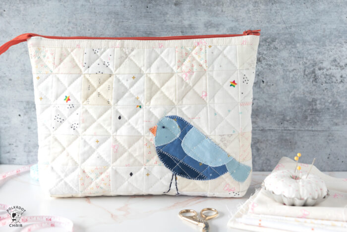 Ivory quilted zip pouch with blue bird on white countertop