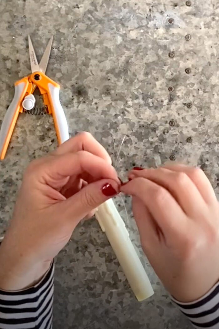 hands tying fishing line to a candle on top of metal table