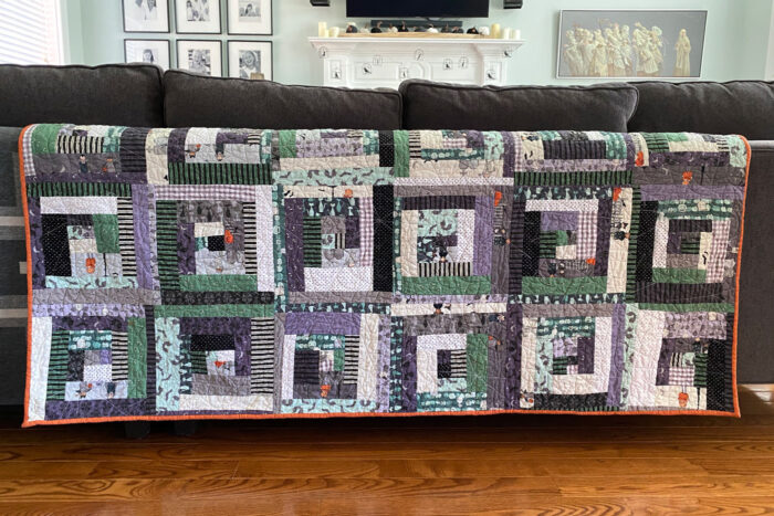 blue, gray purple and white scrappy quilt draped on back of couch