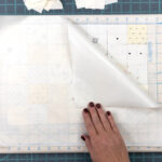 cream and white squares of fabric laid out on portable cutting board with teflon sheet on top