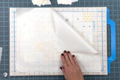 cream and white squares of fabric laid out on portable cutting board with teflon sheet on top