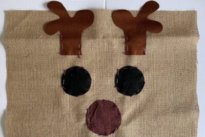 fabric sewn to burlap in shape of reindeer eyes nose and antlers