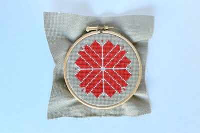 cross stitch red and white ornament on white table in embroidery hoop