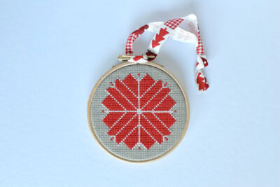 red and white cross stitch ornament with ribbon on white table