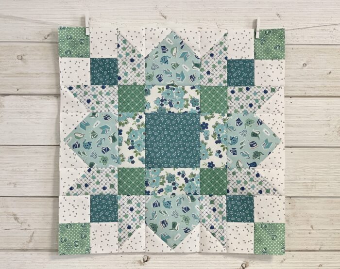 Blue, green and ivory quilt block on white wood table