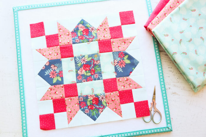 Red, pink, coral and blue quilt block on white wood table