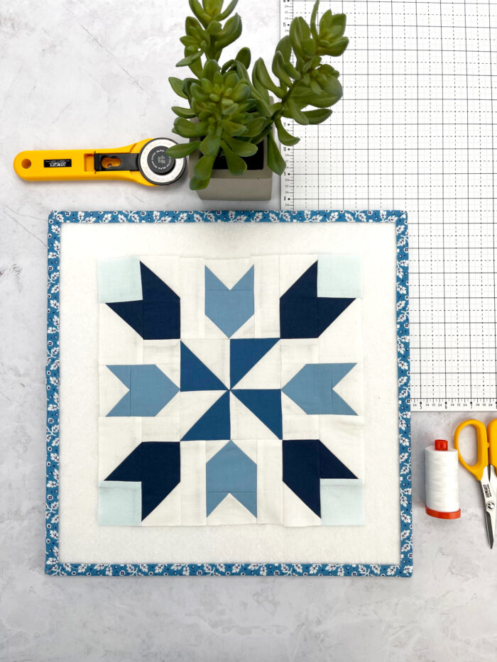 blue and white geometric quilt block on white tabletop with sewing notions