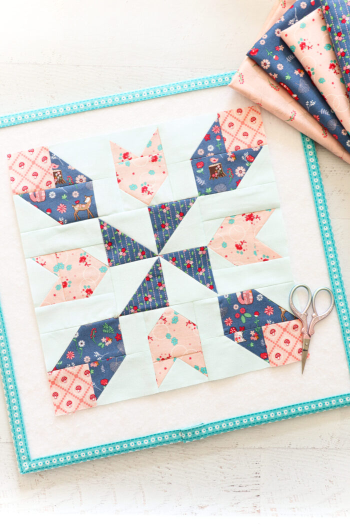 blue and pink quilt block on white mat on table with fabric