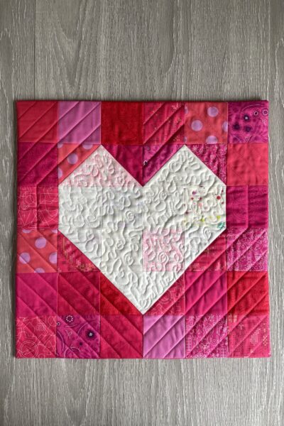red fabric with white heart in center on wood table quilted