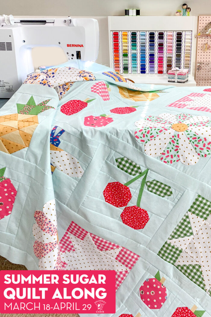 Colorful quilt top on sewing table with sewing machine and thread case in background. 