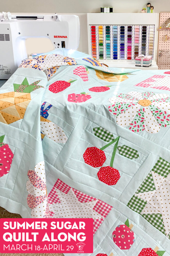 Colorful quilt top on sewing table with sewing machine and thread case in background.