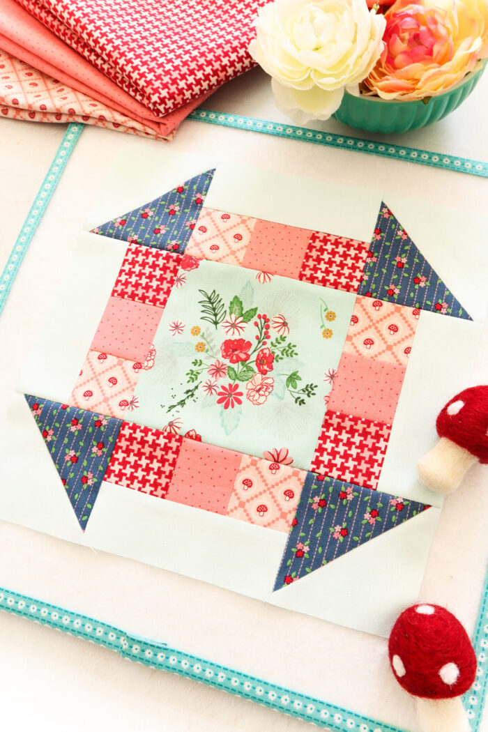 red and blue quilt block on table with fabric and accessories