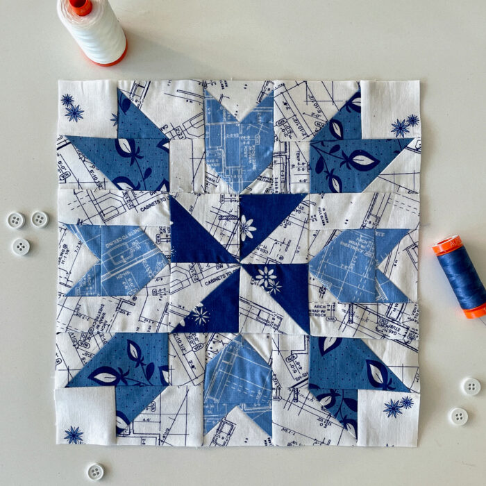 blue and white geometric quilt block on white tabletop with sewing notions