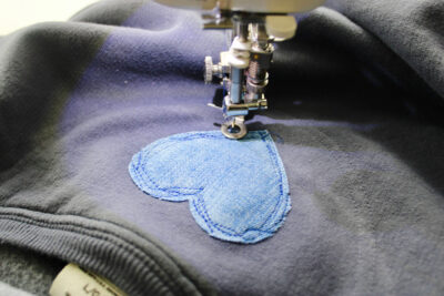 heart being sewn to sweatshirt with sewing machine