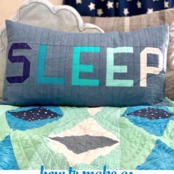 blue and gray patchwork pillow on bed with other pillows