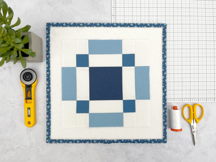 Blue and white quilt block with sewing notions on white cutting mat