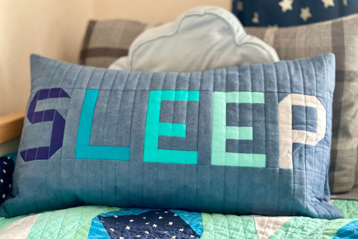 blue and gray patchwork pillow on bed with other pillows