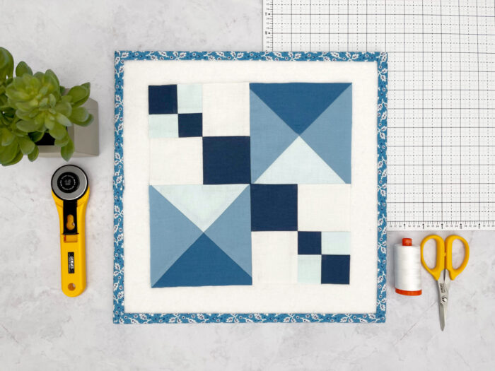 blue and white graphic quilt block on white cutting mat with sewing notions