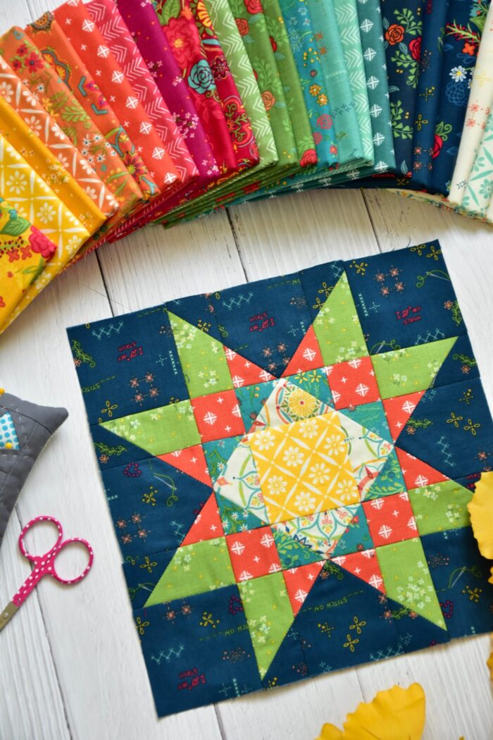 Blue orange and green quilt block on wood table with folded fabrics