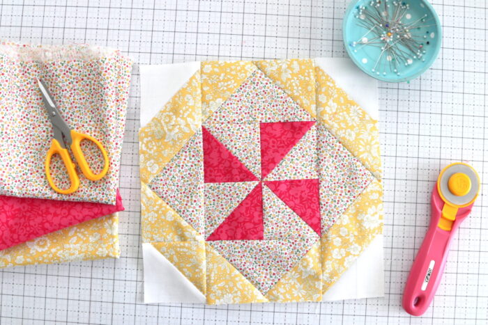 yellow and red quilt block on white cutting mat with scissors and pins