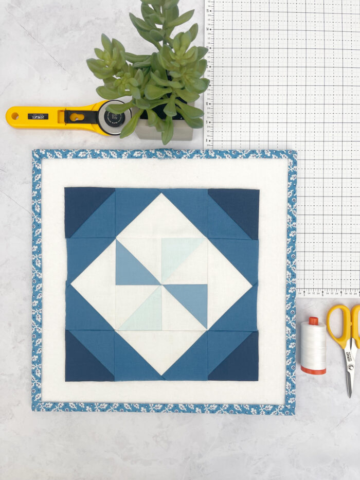 Aqua, blue and white quilt block on white cutting mat with scissors and rotary cutter