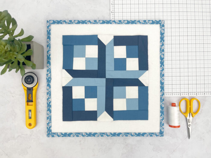 blue and white graphic quilt block on white cutting mat with sewing notions