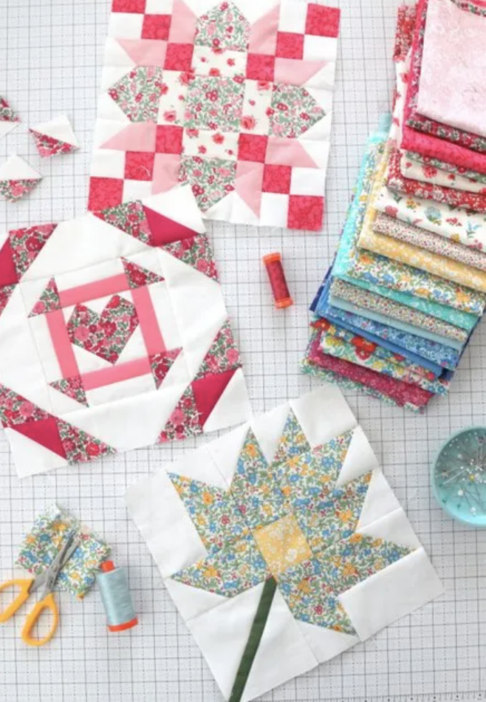 multiple quilt blocks on white cutting mat with a stack of fabric