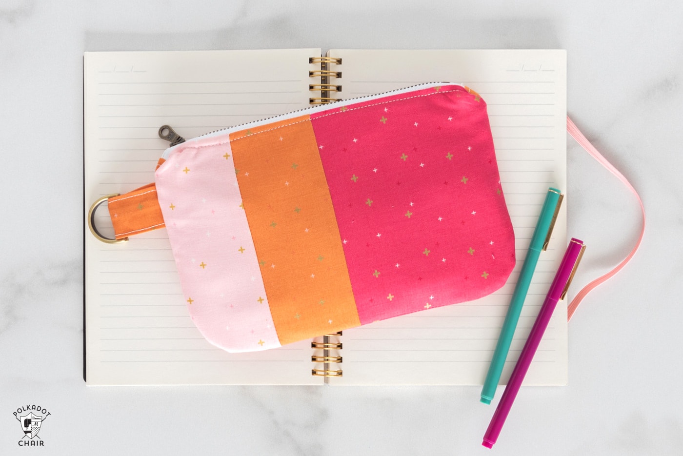 Pink and orange zip clutch on notebook with pens