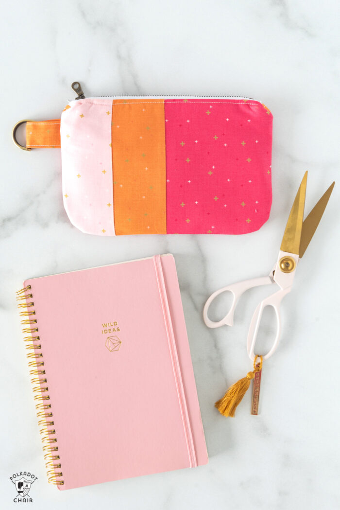 Pink and orange zip clutch on notebook with pens