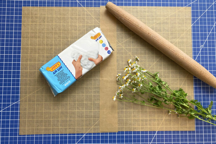 package of clay, rolling pin and flowers on brown paper