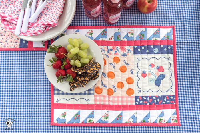 Outdoor table top with blue gingham tablecloth, food, picnic basket and quilted placemats