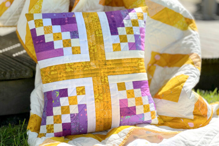 purple and gold union jack patchwork pillow on yellow and white quilt