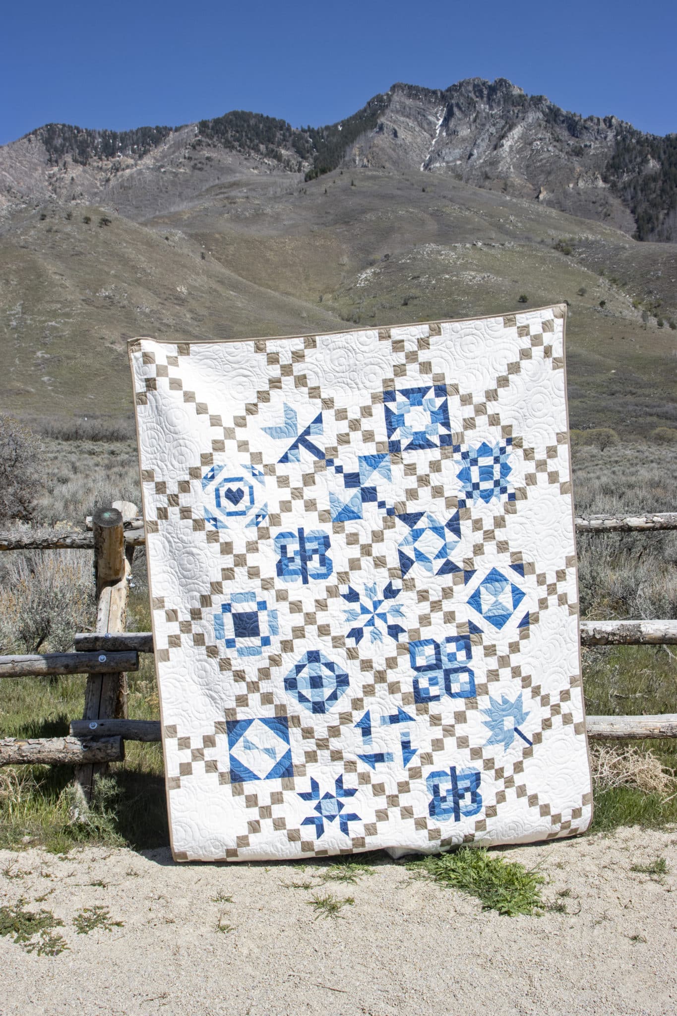blue, white and tan geometric quilt outdoors in front of fence