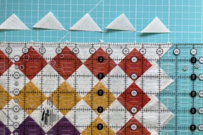 colorful pieced quilt block in red, yellow, green and purple with cutting mat and ruler