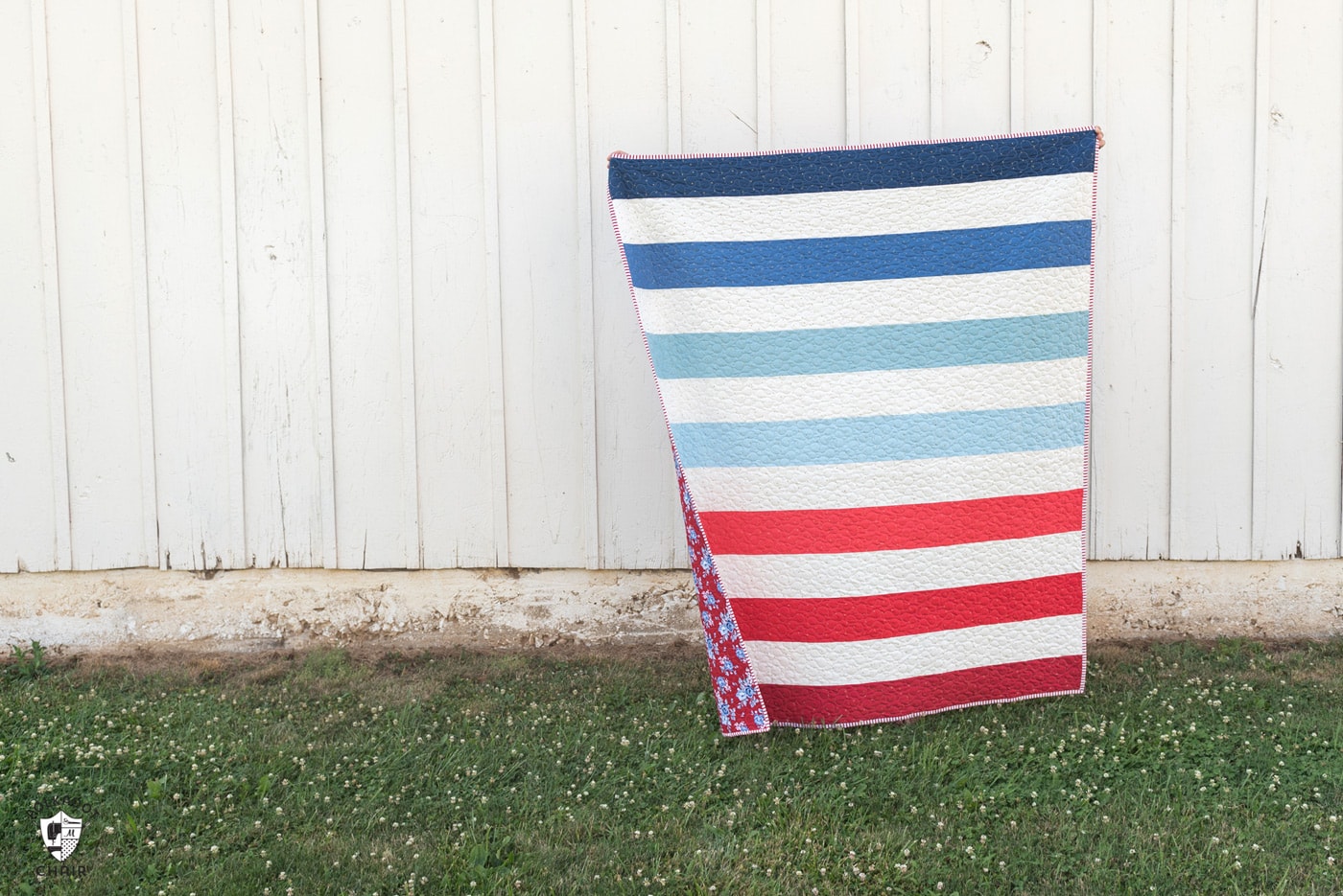 red white and blue striped quilt in front of white barn