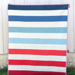 red white and blue striped quilt in front of white barn