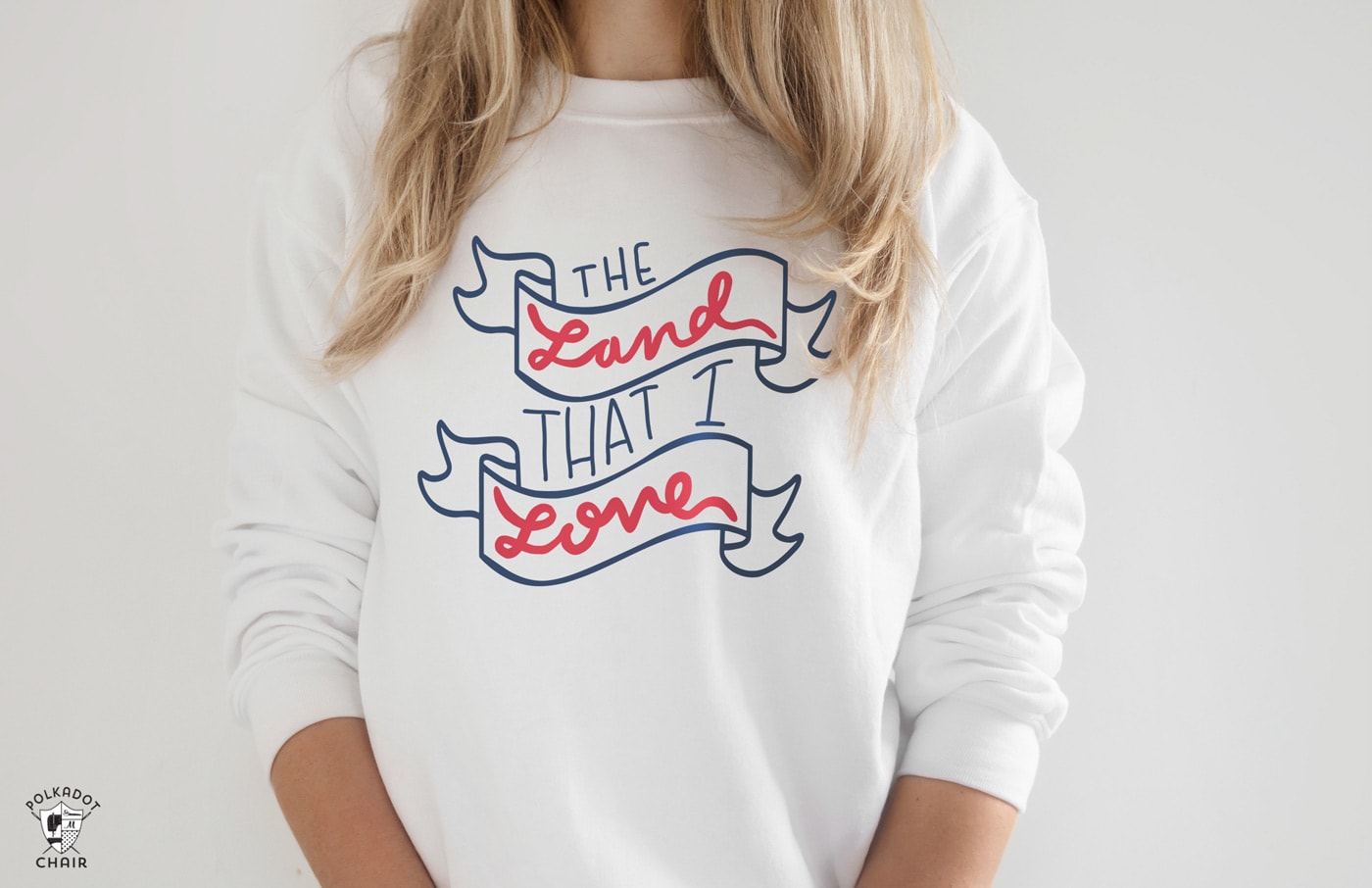 Woman wearing a white sweatshirt with land that i love in red white and blue