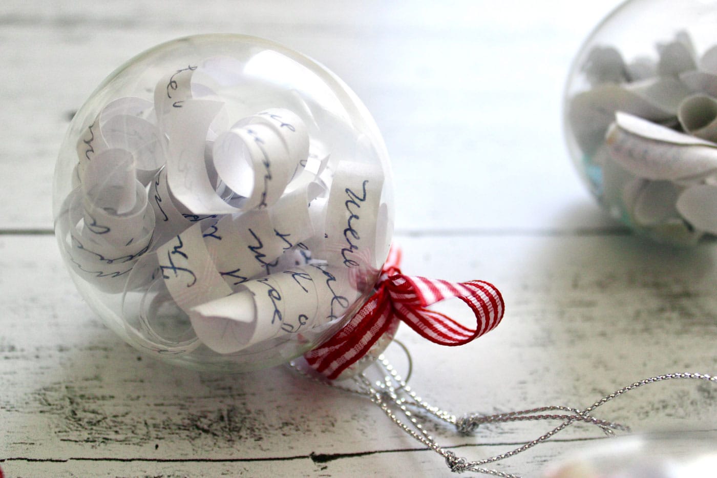 clear christmas ornament filled with paper and red ribbon on white wood table