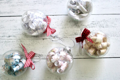 clear christmas ornament filled with paper and red ribbon on white wood table
