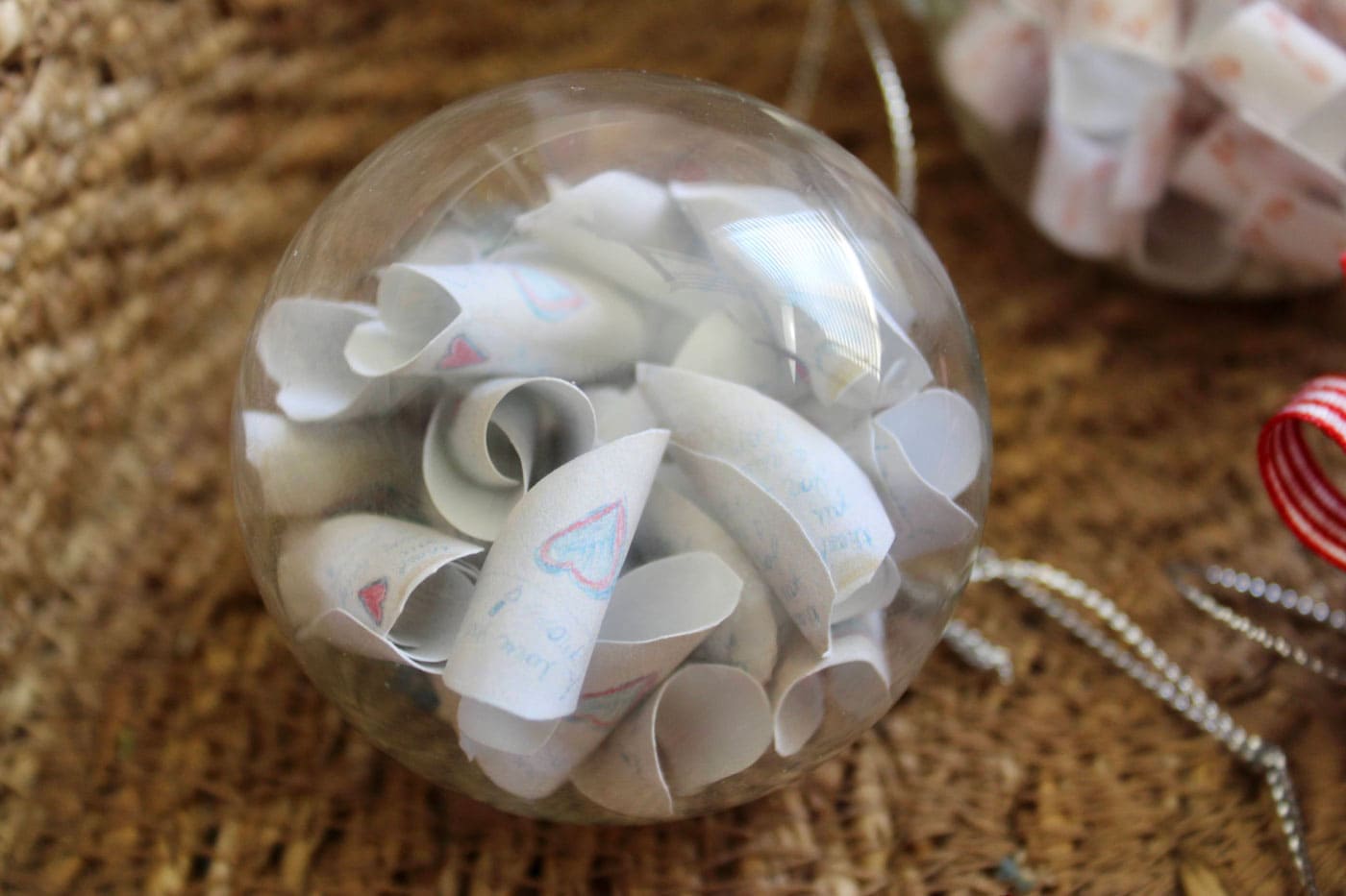 clear christmas ornament filled with paper and red ribbon