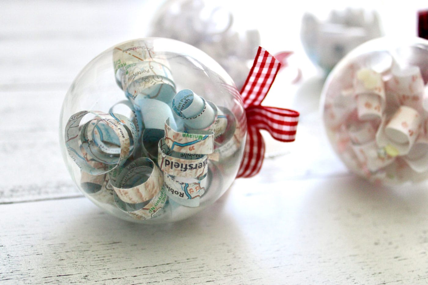 clear christmas ornament filled with paper and red ribbon