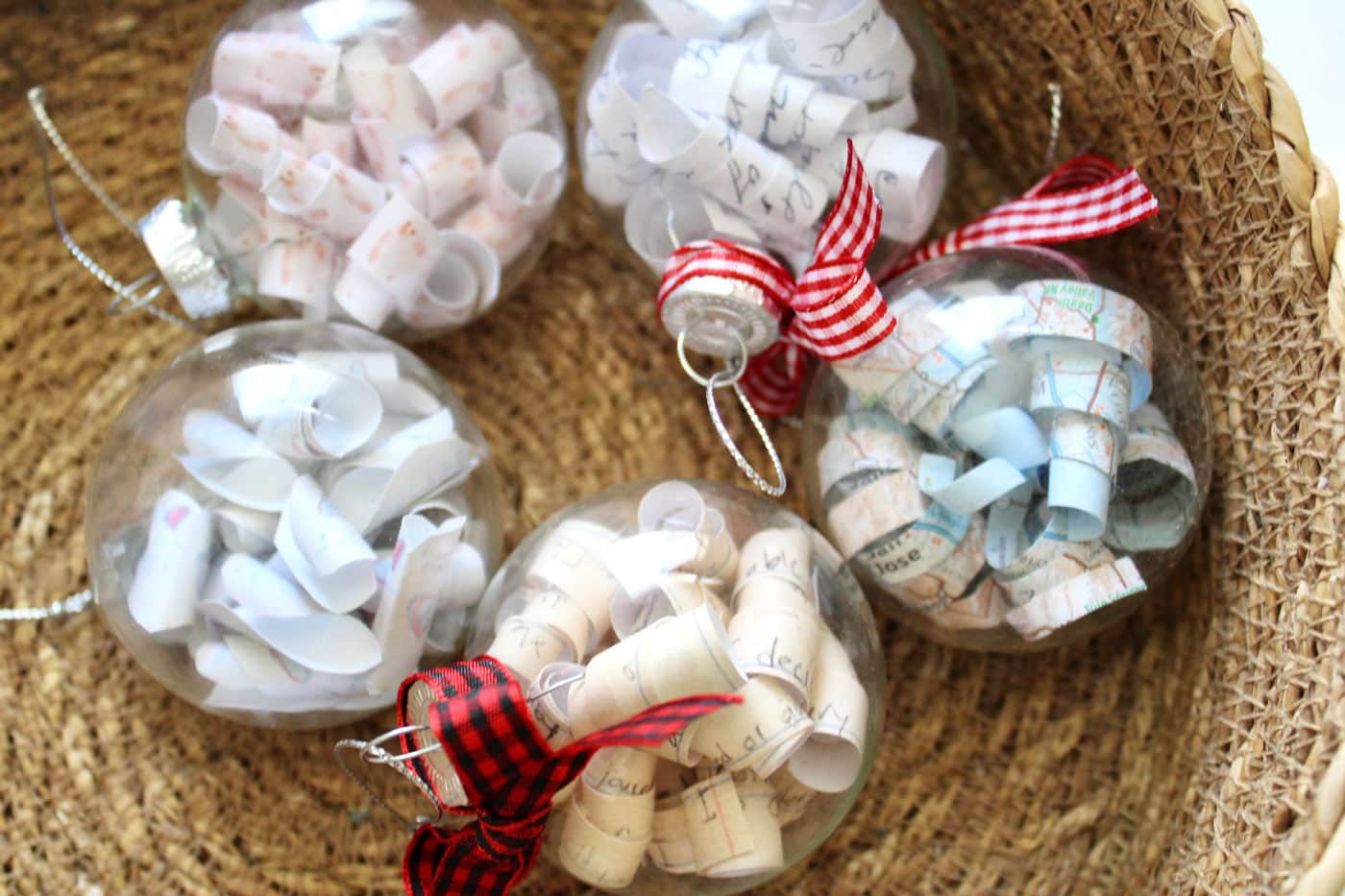 clear Christmas ornaments with paper laying in straw basket