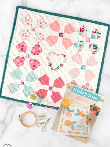 Mini quilt, book and sewing notions on white tabletop