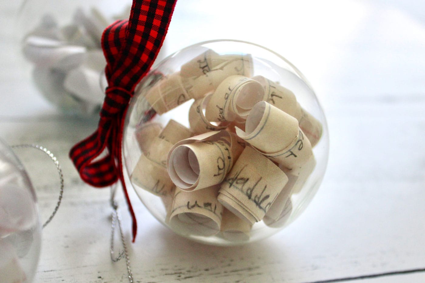 clear christmas ornament filled with paper and red ribbon