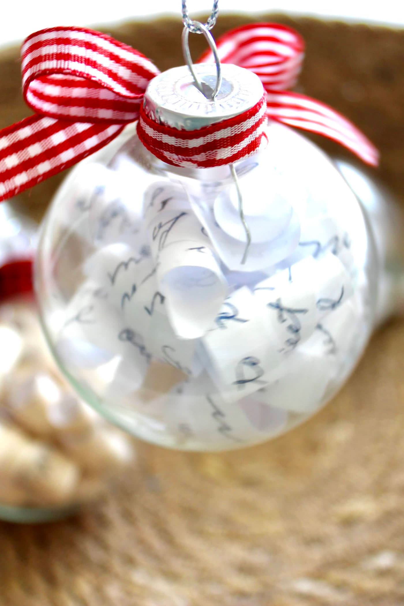 clear christmas ornament filled with paper and red ribbon
