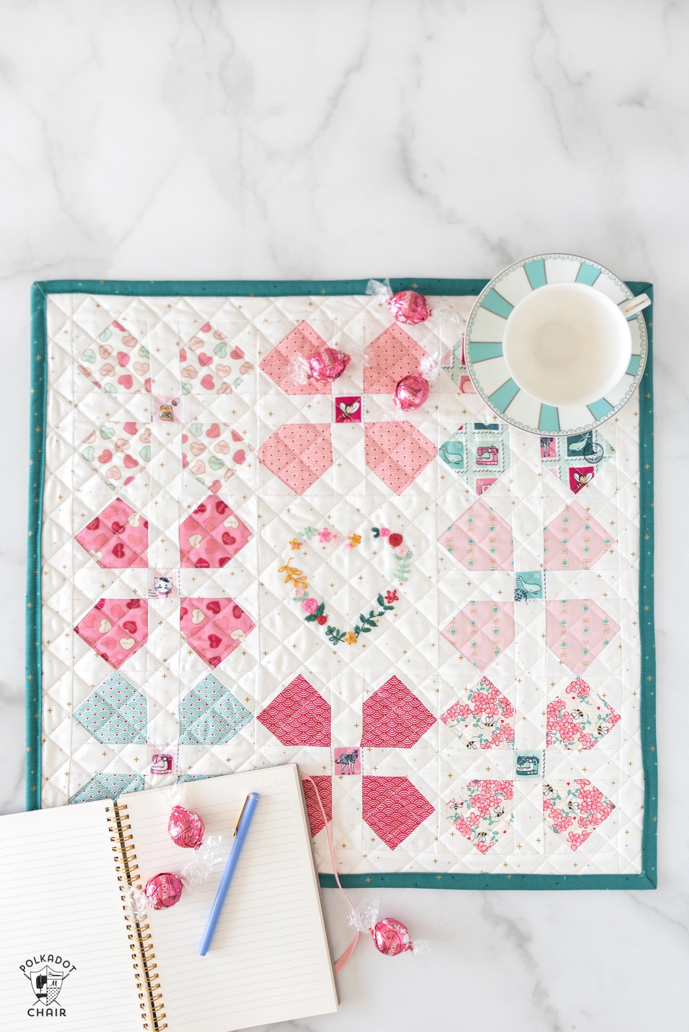 colorful pink and teal mini quilt on white countertop with book and candy