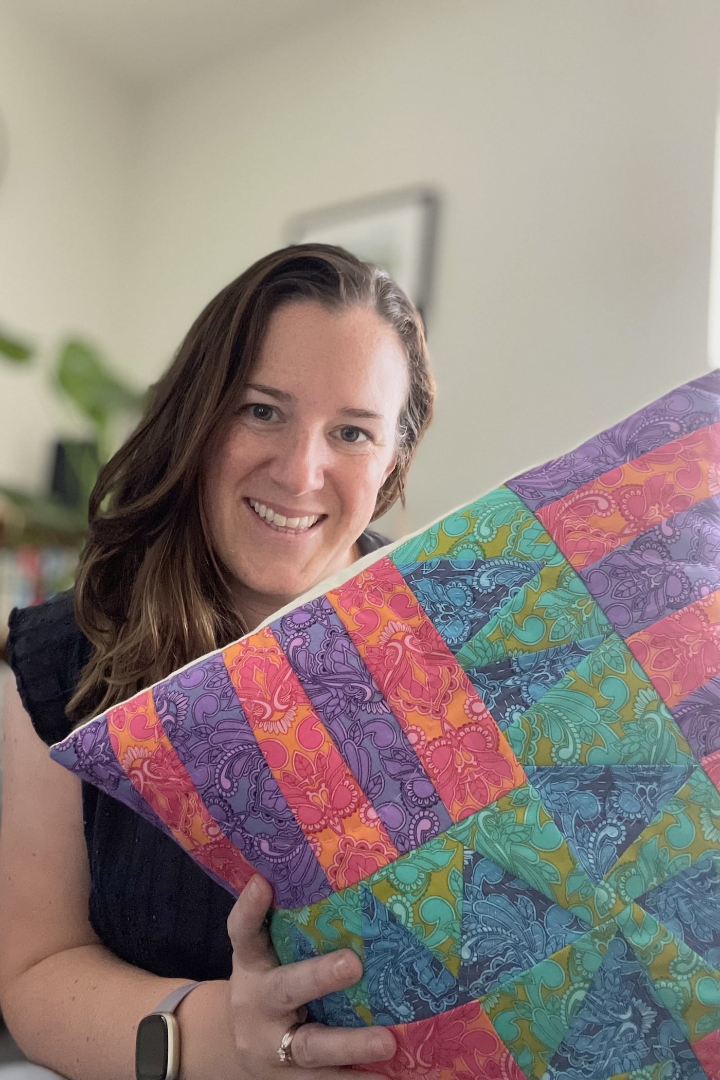 woman holding Blue, green, purple and red patchwork pillow on couch