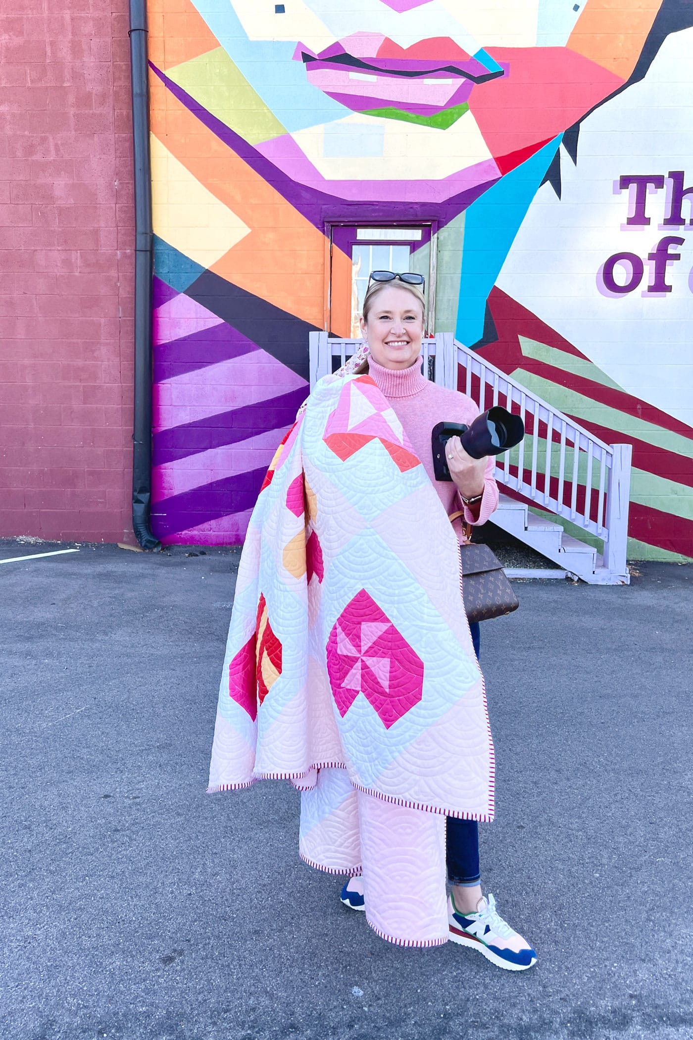 woman photographing quilt in front of mural