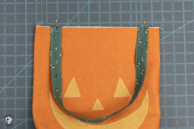 green bag straps pinned to front of orange tote bag