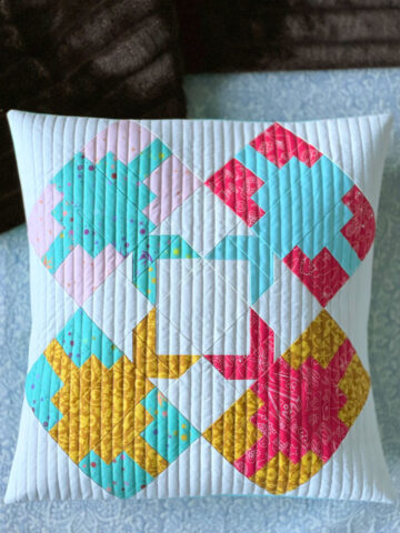 blue, pink and yellow pieced pillow, quilted on bed